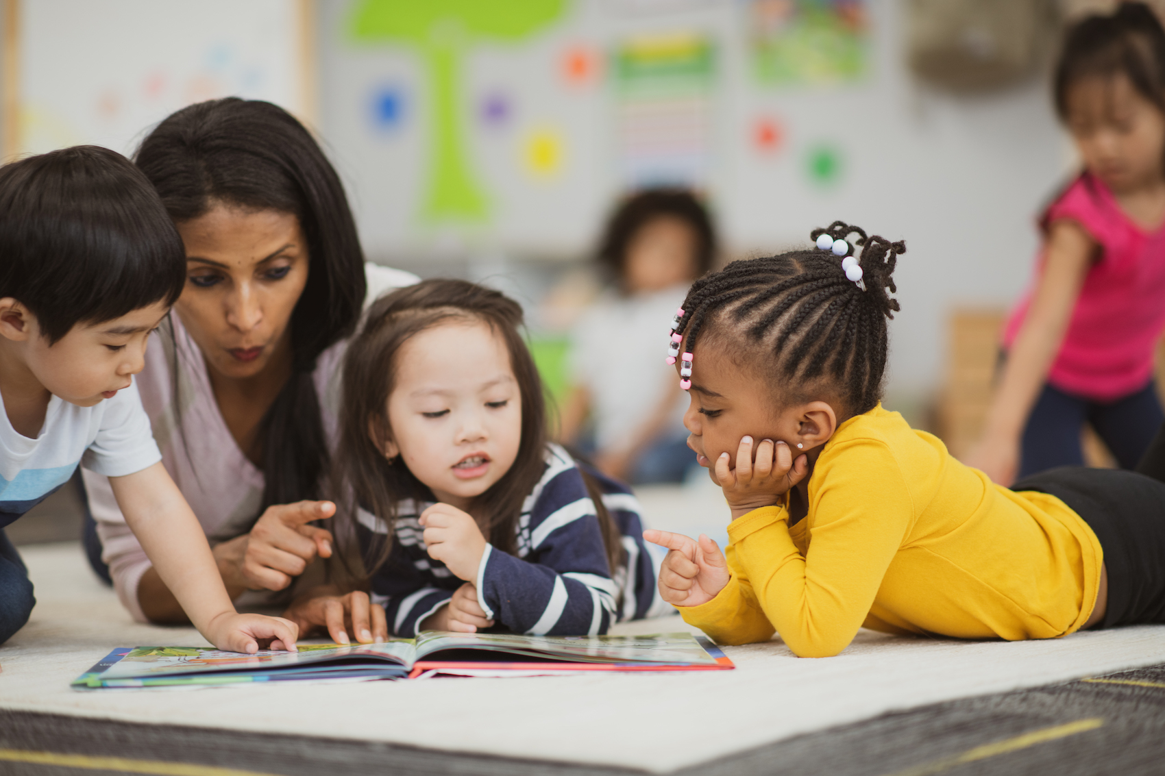 A few children lay on the ground with a teacher actively engaged in reading a book