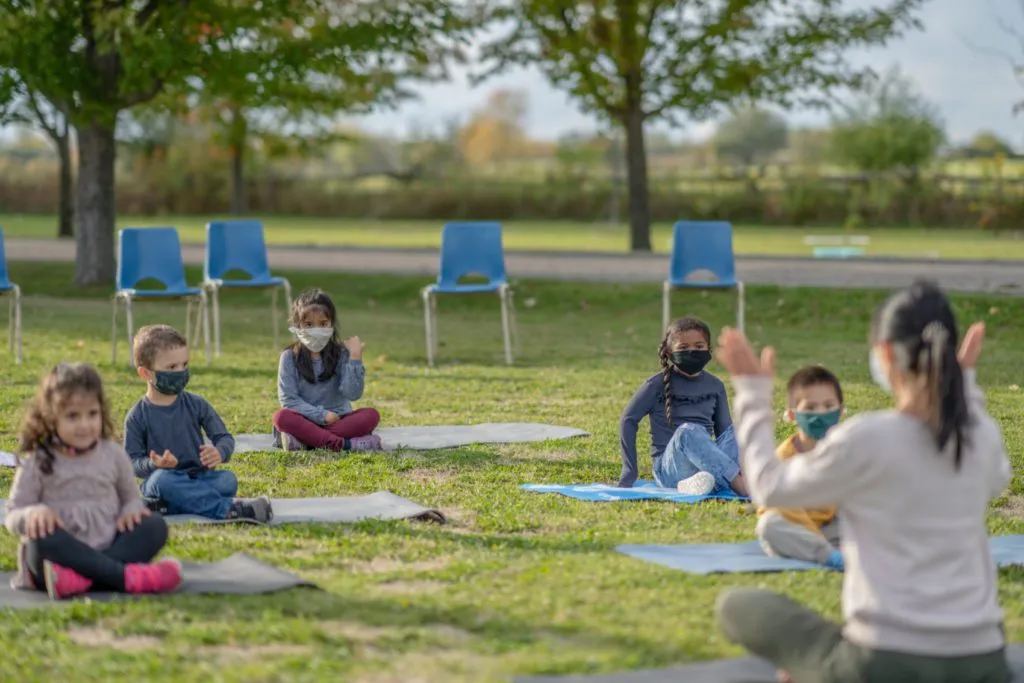 Teacher leading a class of young children wearing masks outdoors