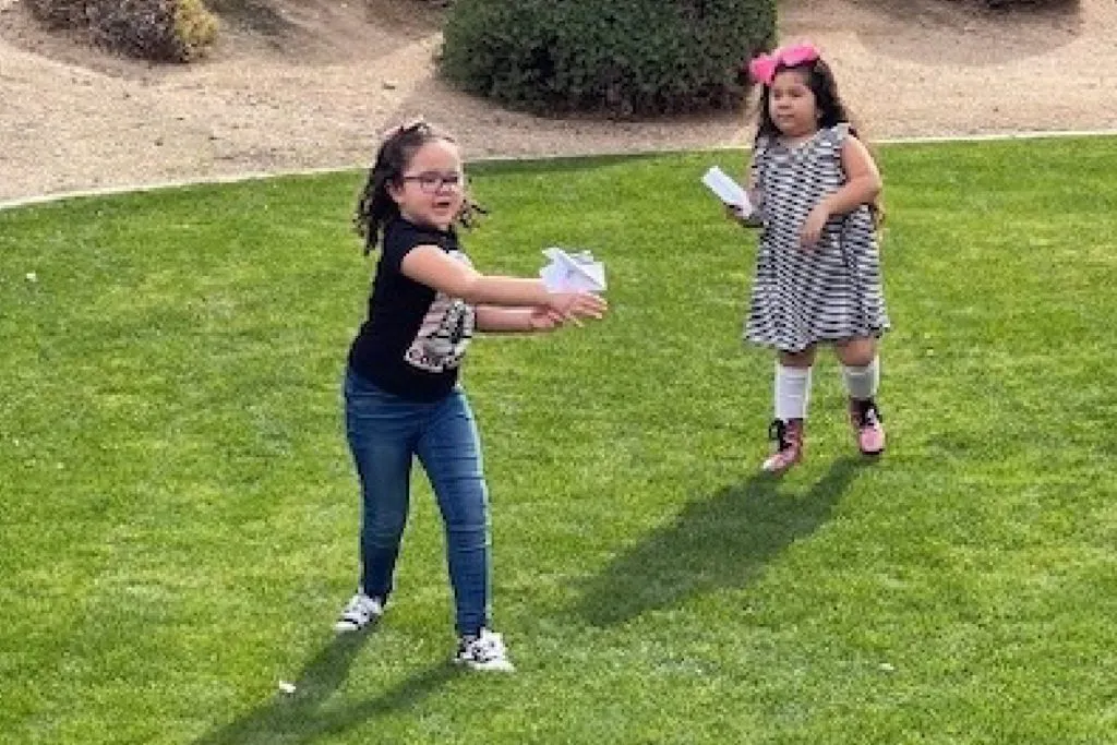 two young children playing outdoors with paper planes