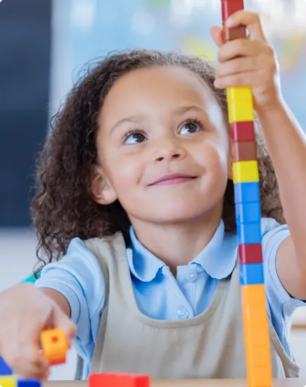 smiling child in her classroom using plastic interlocking cubes