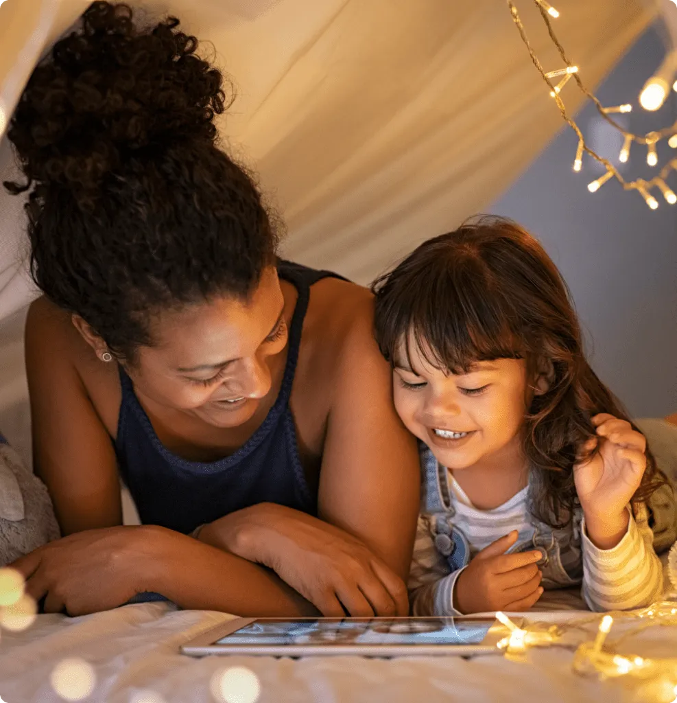 A mother and small child reading on a tablet under a homemade fort.