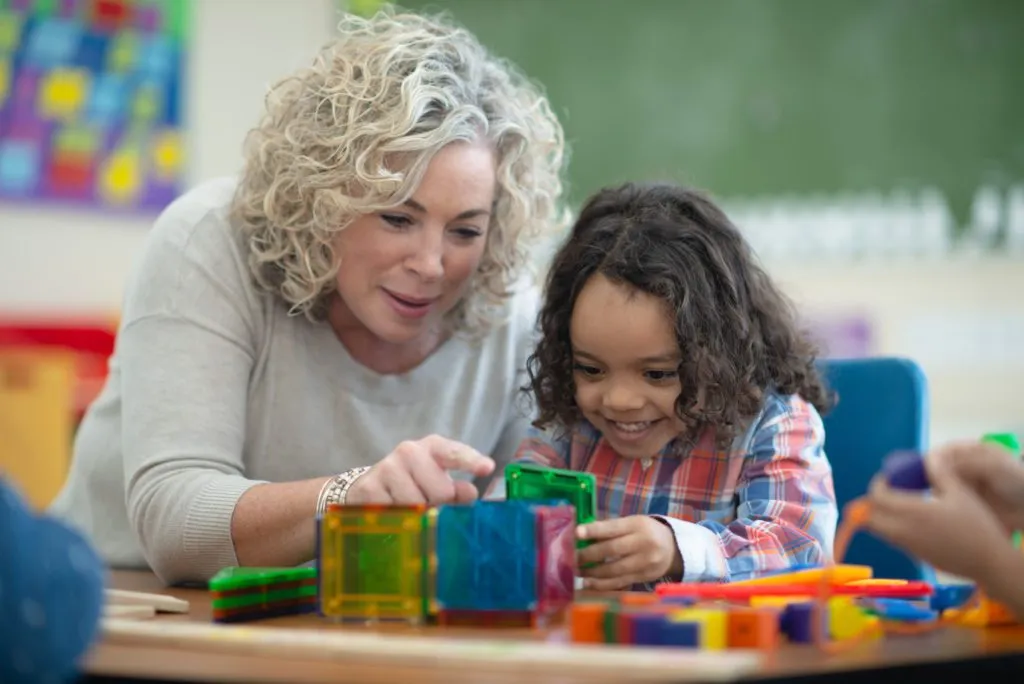 Teacher and preschool child in the classroom building a cube and They are focused but also smiling and having fun.