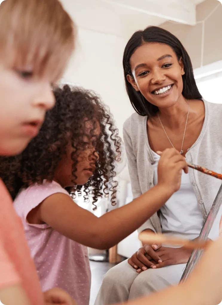 two children painting teacher overlooking smiling