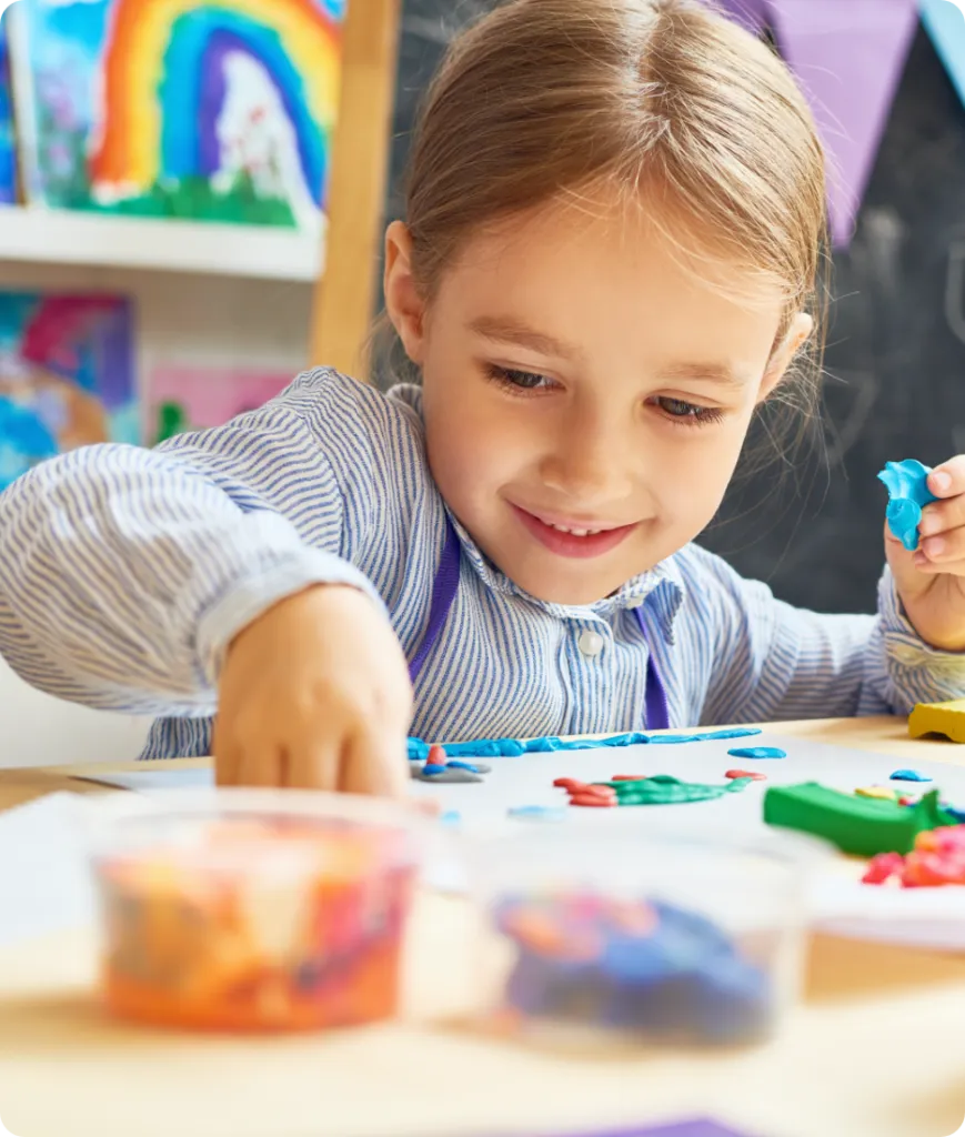 happy Caucasian kindergarten girl playing with clay in classroom