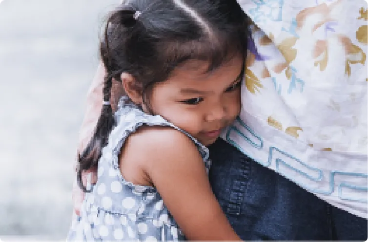 sad young girl holding on to parents leg